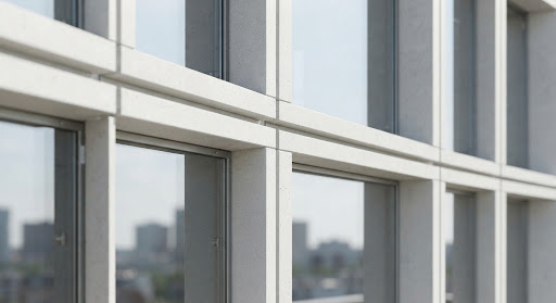 A close view of architectural concrete and glass panels meeting in clean parallel lines under bright daylight.
